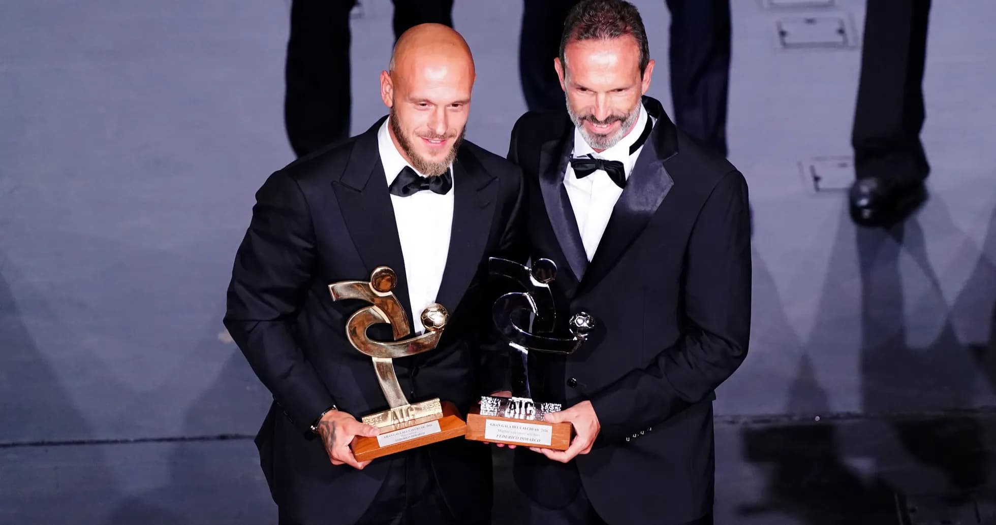 Deux hommes en costume tenant des trophées sur scène
