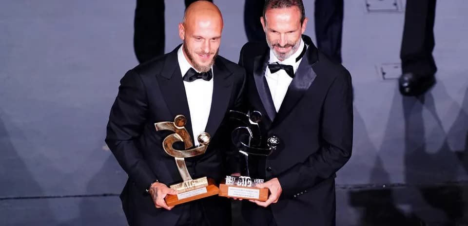 Deux hommes en costume tenant des trophées sur scène
